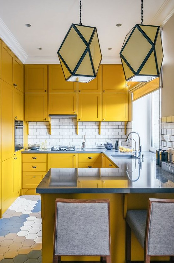 a mustard kitchen with grey stone countertops and grey stools, a white subway tile backsplash anbd geometric pendant lamps