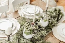 a neutral rustic Christmas table with white woven placemats, a greenery runner, tall candles and white porcelain