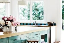 a pretty beach-inspired kitchen with a turquoise kitchen island with butcherblock countertops, a wooden stool, white kitchen cabinetry with butcherblock countertops and striped tiles