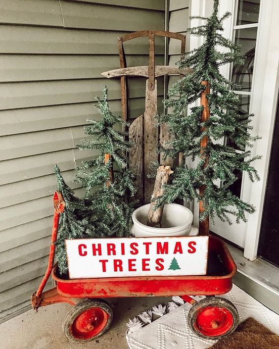 a red cart with a sign, three Christmas trees in buckets is a nice rustic porch decoration