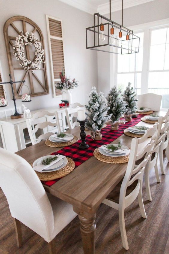 a red plaid runner, flocked Christmas trees in burlap, candles, woven placemats and evergreens on each place setting