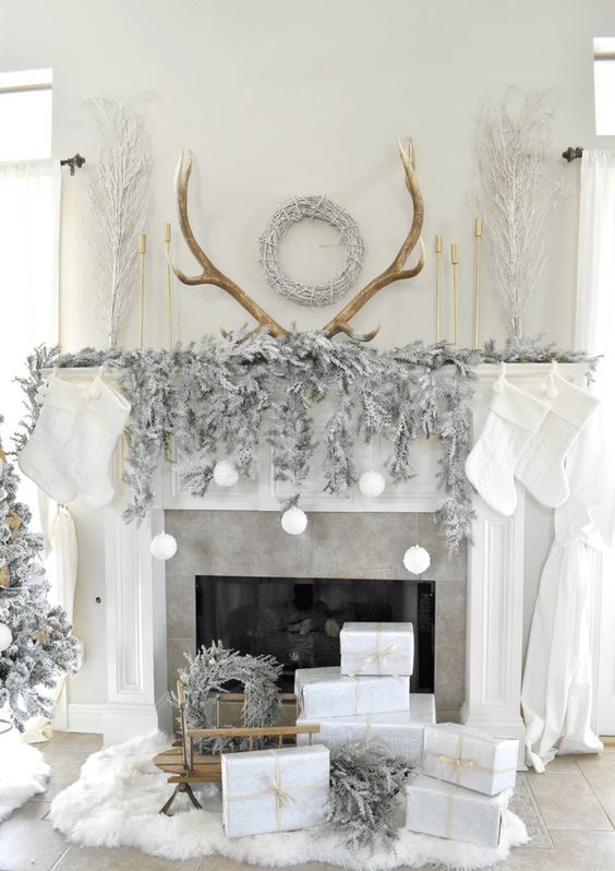a refined Christmas mantel with a sivler evergreen garland, white ornaments, antlers, white stockings and white gift boxes
