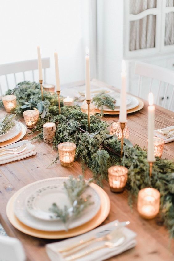 a refined rustic Christmas table with an evergreen runner, lots of candles, gilded chargers and evergreen touches