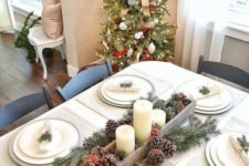 a simple neutral Christmas tablescape with silver chargers, white plates, evergreens and pinecones, berries and candles