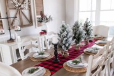 a simple rustic Christmas table with a plaid runner, woven placemats, snowy Christmas trees and evergreens