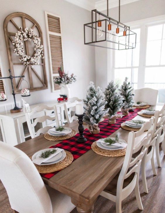 a simple rustic Christmas table with a plaid runner, woven placemats, snowy Christmas trees and evergreens