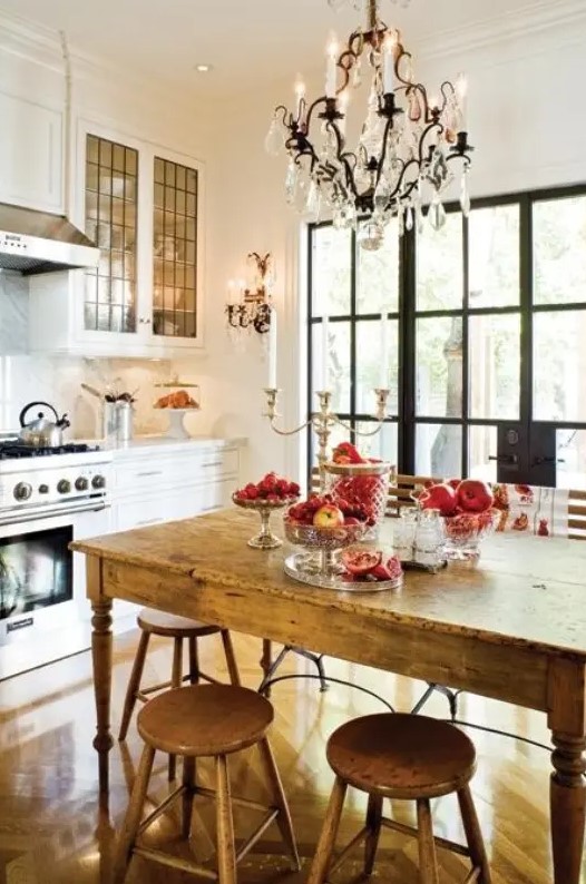 a small eclectic kitchen with white farmhouse cabinets, a vintage wooden dining set and a large crystal chandelier