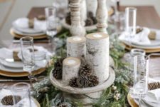 a snowt rustic Christmas table with a flocked evergreen runner, pinecones, branch candleholders, pinecone napkin rings