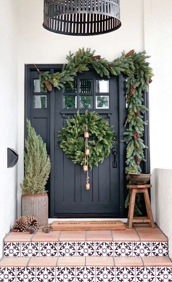 a very natural Christmas porch with a tree, pinecones, an evergreen wreath with bells and an evergreen garland with pinecones