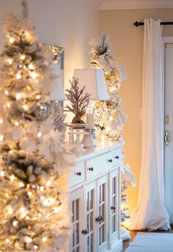 elegant and chic white Christmas decor with flocked Christmas trees decorated with lights and paper garlands, mini flocked trees and candles