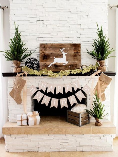 rustic fireplace styling with Christmas trees wrapped in burlap, burlap stockings, a paper garland, a fabric leaf one and a deer sign