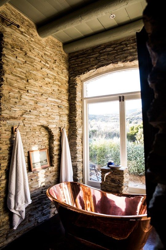 a beautiful bathroom with stone walls, a copper bathtub and towels plus a gorgeous view featured