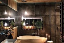 a beautiful moody bathroom clad with wood and with dark tiles, with a chic bathtub, a floating wood slab vanity and candles around