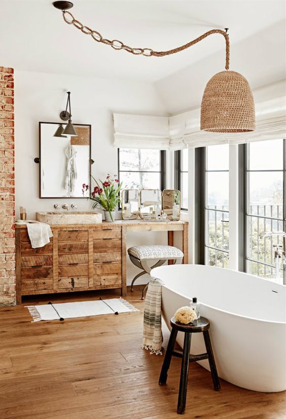 a catchy bathroom with a glazed wall, a reclaimed wood vanity and a pendant lamp, an oval tub and an exposed brick pillar