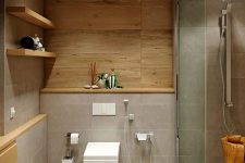 a chic minimalist bathroom clad with grey tiles and wood, with a shower space and a tree stump, open shelves for storage