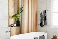 a contemporary bathroom clad with large scale white tiles and wooden slabs, with a wooden floor, a chic tub and some lovely decor
