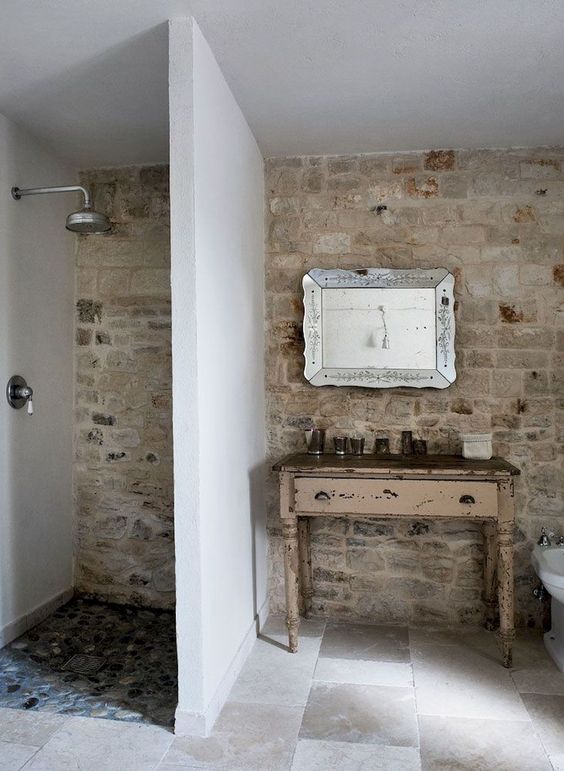 a farmhouse bathroom with a stone wall, tiled floor, a shaby chic vanity and a gorgeous refined mirror