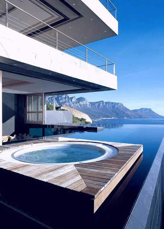 a floating wooden deck in the water with a jacuzzi, a stunning view of the mountains and sea