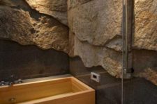 a gorgeous contemporary bathroom done with rough stone walls covered with glass and a wooden bathtub
