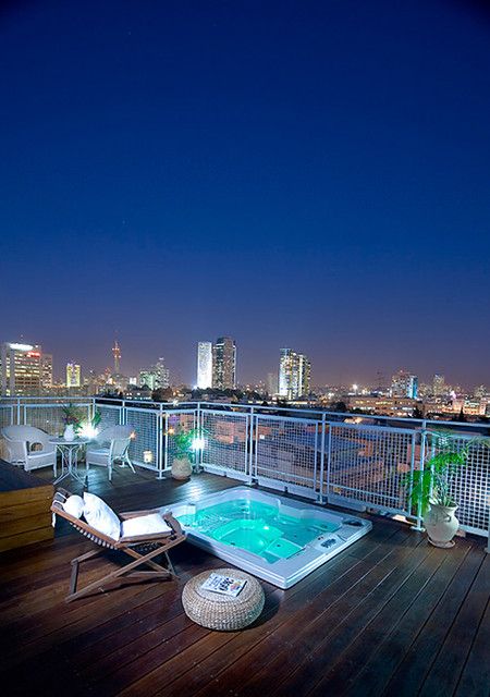 a jacuzzi on the deck, with a folding chair, a pouf, some greenery and a stunning view of the big city is amazing
