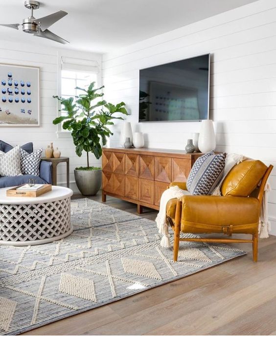 A mid century modern living room with mustard and blue furniture, an inlay sideboard and a rug with boho embroidery