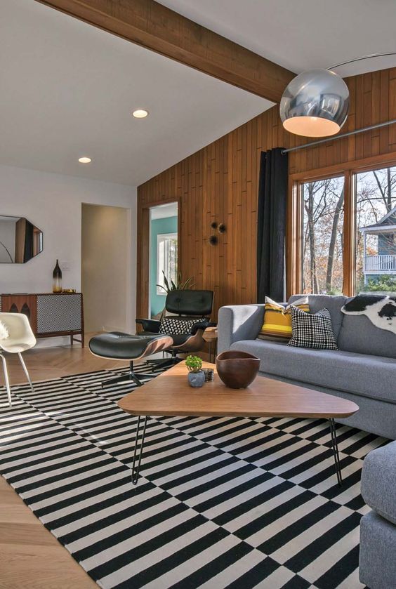 a mid-century modern living space with a striped rug takign over it, black, white and grey furniture, lamps and a hairpin leg table