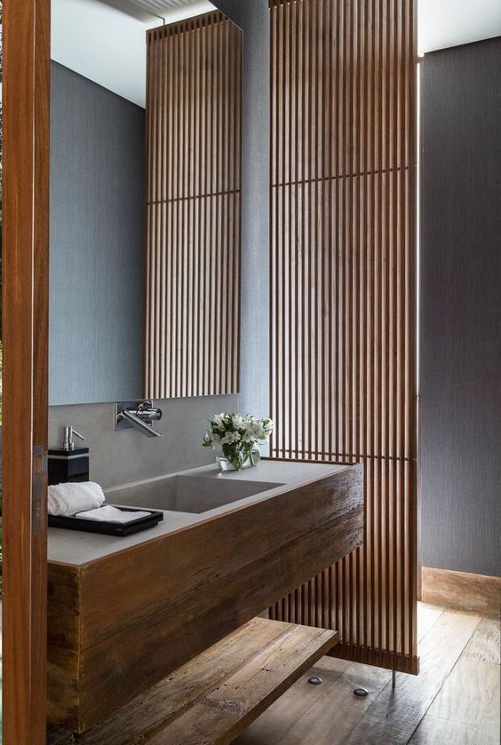 A minimalist bathroom with a planked screen, a wooden vanity with a built in sink, a shelf and a wooden floor is a chic space