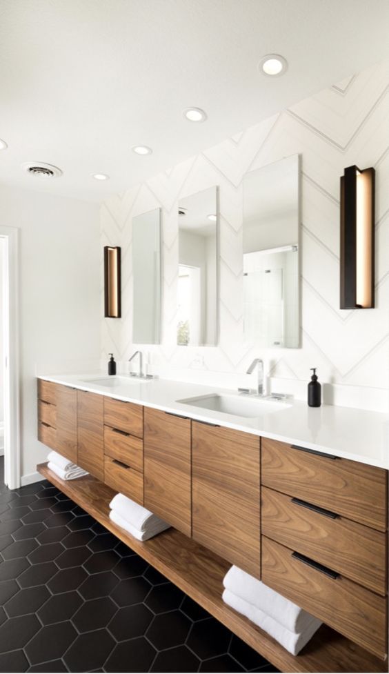 A modern bathroom done with black and white tiles, with a stained wooden vanity and a trio of mirrors, with built in lights