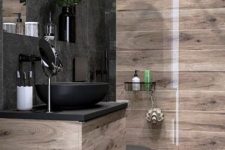 a moody bathroom clad with light stained wood and with black tiles, a chic vanity with a black sink and black fixtures is a lovely space