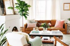 a neutral living room with a brown leather sofa, creamy furniture, potted greenery, mirror and a firewood storage space