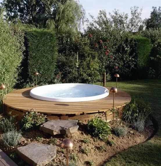 a round wooden deck with a jacuzzi and green walls all around to keep privacy