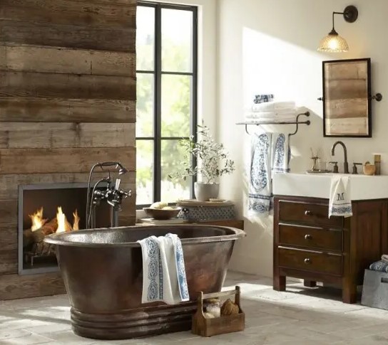 a rustic barn bathroom with a reclaimed wooden wall, wooden furniture, a built-in fireplace and a vintage metal bathtub