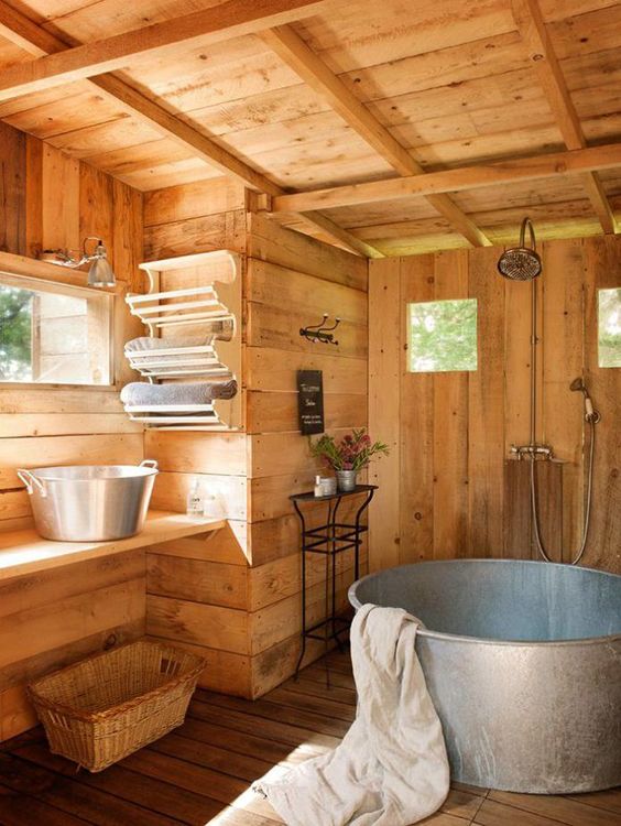 a rustic bathroom of wood, with a galvanized steel bathtub, a vanity with matching steel sinks, some windows