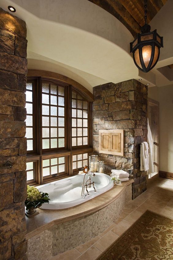 A rustic bathroom with rough stone walls, a built in bathtub clad with tiles and a vintage lamp
