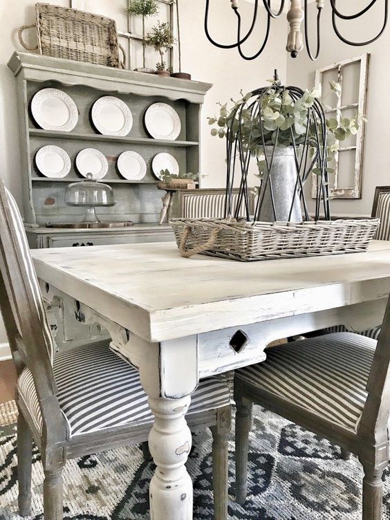 a rustic meets shabby chic dining room with a grey buffet, mismatched neutral furniture, baskets and greenery