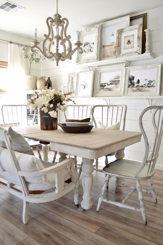 a shabby chic dining room with white shiplap walls, mismatched furniture, a large gallery wall and a vintage chandelier
