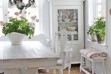 a shabby chic meets rustic white dining room with elegant vintage furniture, an old chandelier and potted plants and blooms