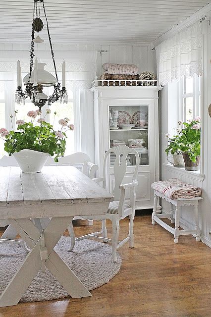 a shabby chic meets rustic white dining room with elegant vintage furniture, an old chandelier and potted plants and blooms