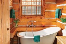 a small cabin bathroom clad with wood, with wooden beams, a wooden vanity, a clawfoot tub and bold textiles