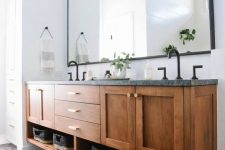 a stylish modern bathroom with a black tiled floor, a floating wooden vanity with a stone countertop, black fixtures and baskets for storage