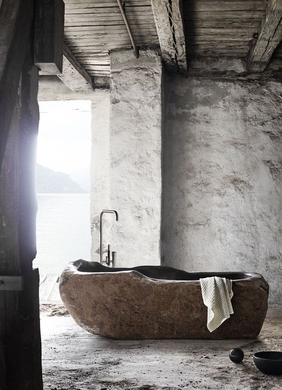 A wabi sabi bathroom with plaster walls and a bathtub cut out of a stone slab is a unique idea to go for