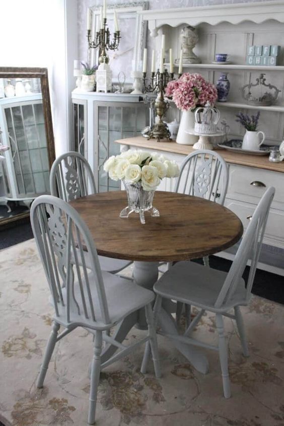 A welcoming shabby chic dining room with off white furniture, candles in candelabras, a large mirror and blooms