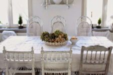 an airy shabby chic dining room with stylish furniture, lace linens, white porcelain and some moss