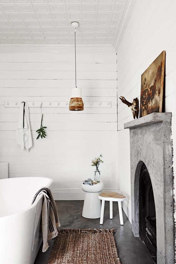 an eclectic bathroom with white planked walls, a fireplace with a concrete mantel, an oval tub, pendant lamps and a jute rug
