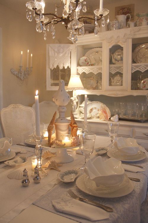 an elegant coastal meets shabby chic dining room with white furniture, a crystal chandelier, candles, starfish, seashells and lace