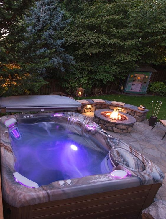 an outdoor jacuzzi with a fire pit next to it, with a stone bench and lights compose a cool outdoor rest zone