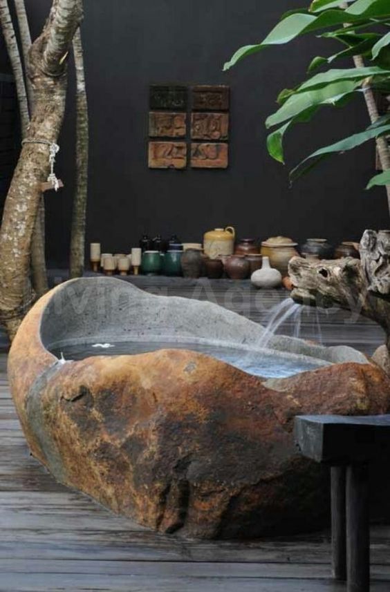 an outdoor tropical bathroom with a bathtub cut out of a stone slab, lots of pots and potted plants