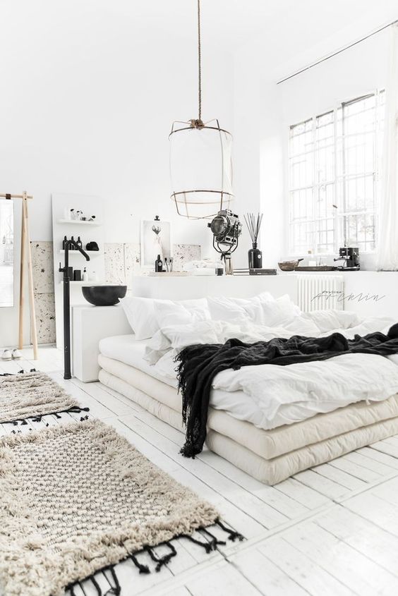 a Scandinavian bedroom with a bed of mattresses, pendant lamps, woven rugs and a bathroom in here