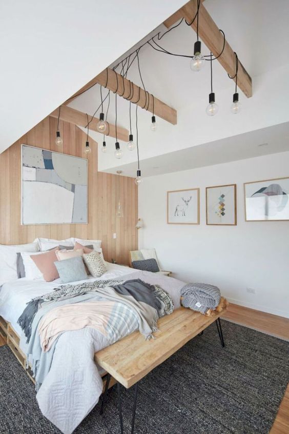 a Scandinavian bedroom with a wooden bed and bench, some bulbs hanging down and pastel touches