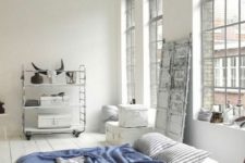 a Scandinavian sleeping space with oversized windows, a shelving unit on casters, a comfy bed and some wooden furniture